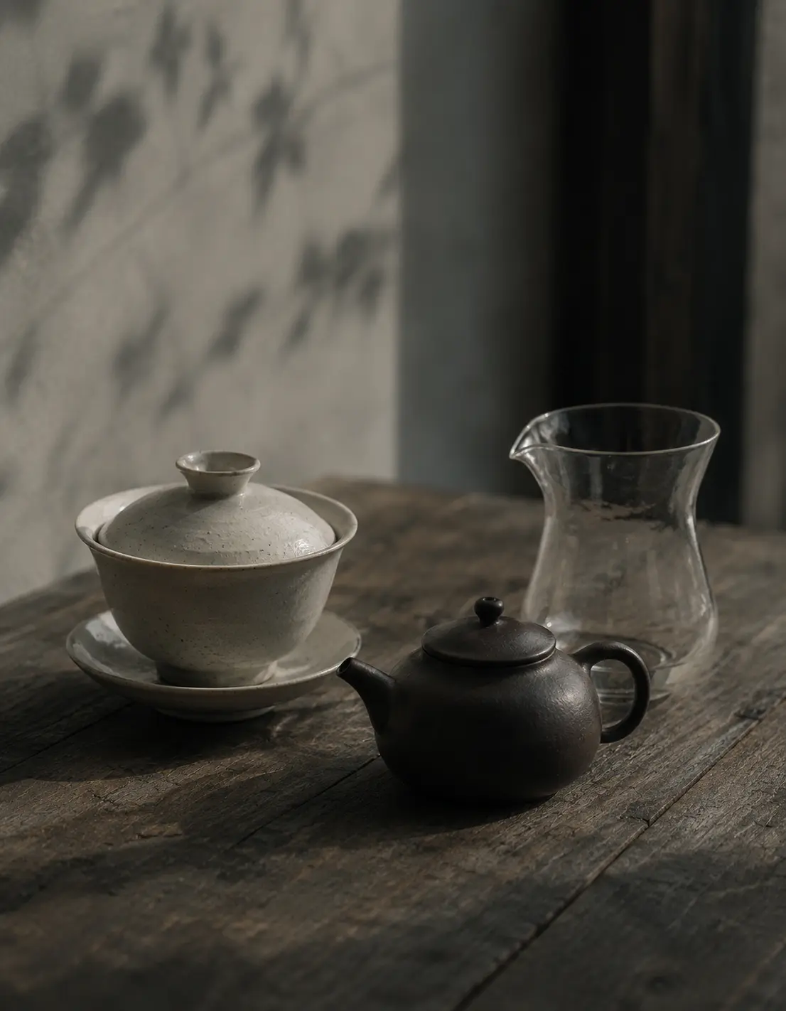 White porcelain gaiwan, dark clay Jian Shui teapot, and glass pitcher representing three teaware traditions